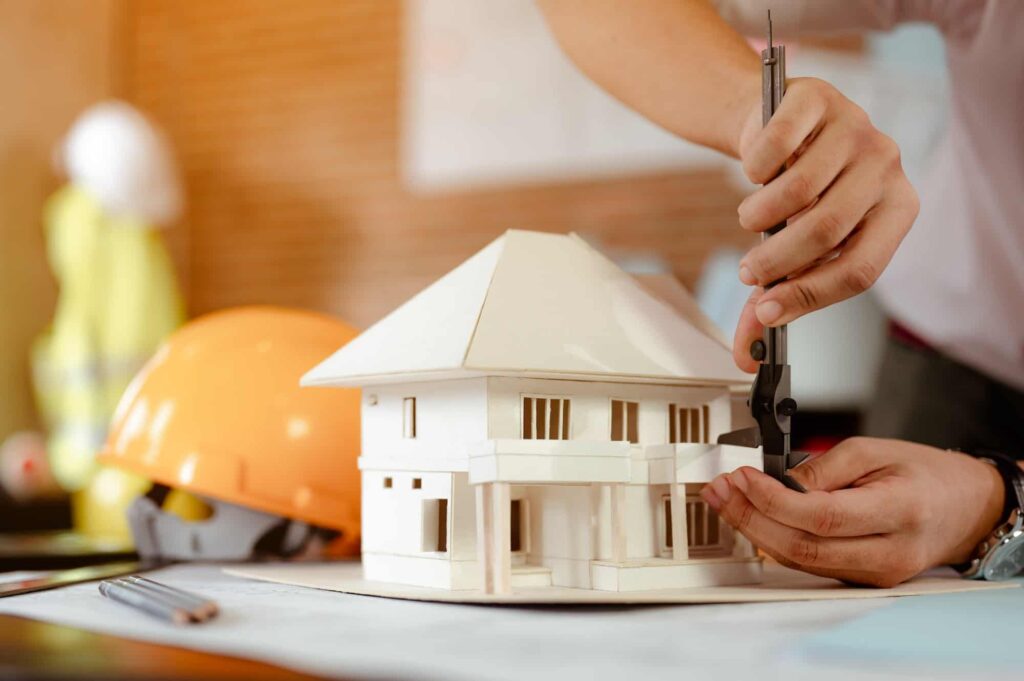 close up of male architect hands measuring and making model house on the desk at sunset